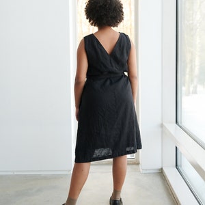 May include: A black linen wrap dress with a V-neckline and a tie belt. The dress is knee-length and has a relaxed fit.