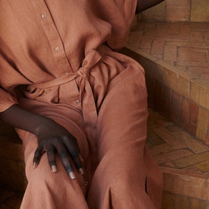 Puede incluir: Un vestido de lino terracota con botones en la parte delantera y un cintur&oacute;n de lazo. El vestido tiene un corte holgado y una falda fluida.