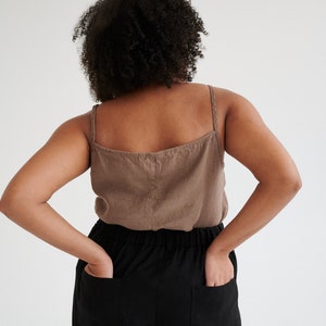 May include: A woman wearing a brown linen tank top and black linen pants with pockets. The pants have an elastic waistband.