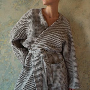 May include: A gray waffle weave robe with a self-tie belt and a patch pocket. The robe is made of a soft, absorbent material and is perfect for lounging around the house.