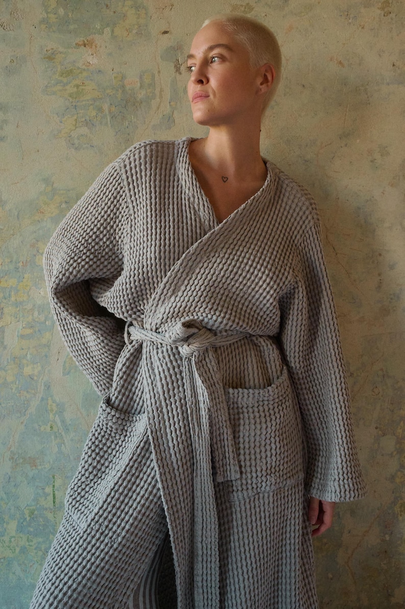 May include: A gray waffle weave robe with a self-tie belt and a patch pocket. The robe is made of a soft, absorbent material and is perfect for lounging around the house.