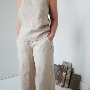 May include: A beige linen pantsuit with a sleeveless top and wide-leg pants. The pants have pockets.