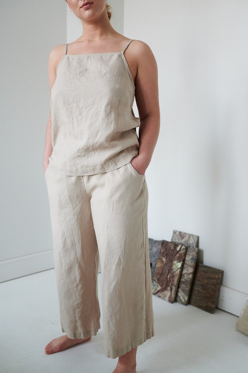 May include: A beige linen pantsuit with a sleeveless top and wide-leg pants. The pants have pockets.