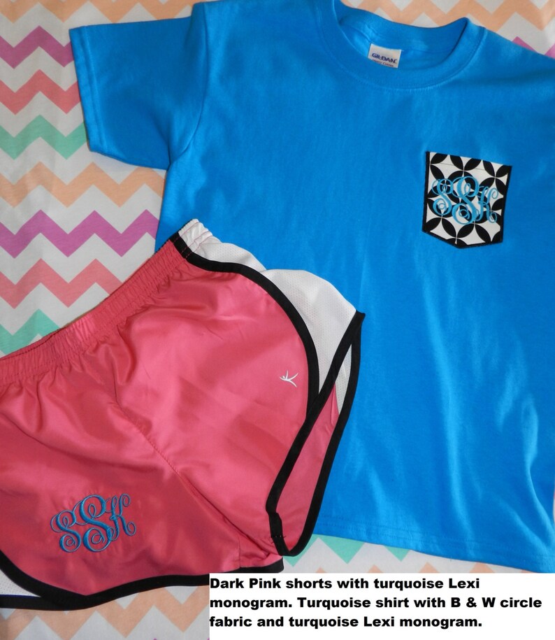 Puede incluir: Shorts de running rosa oscuro con un monograma turquesa y una camiseta turquesa con un bolsillo circular blanco y negro y un monograma turquesa.