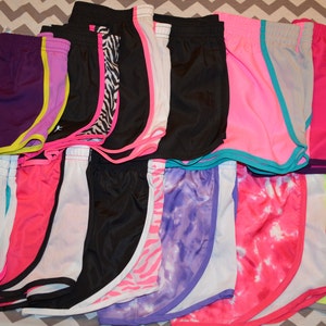 Puede incluir: Una colecci&oacute;n de 15 pares de pantalones cortos deportivos en varios colores y patrones, incluyendo rosa, morado, azul, negro, blanco y amarillo. Los pantalones cortos tienen un ribete de color contrastante alrededor de los bordes.