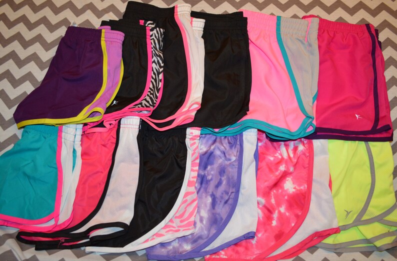 Puede incluir: Una colecci&oacute;n de 15 pares de pantalones cortos deportivos en varios colores y patrones, incluyendo rosa, morado, azul, negro, blanco y amarillo. Los pantalones cortos tienen un ribete de color contrastante alrededor de los bordes.