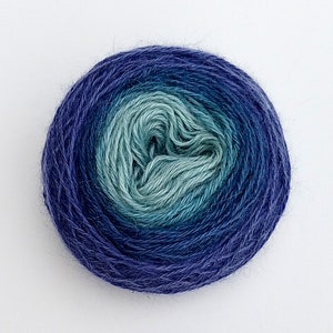 Pode incluir: Uma bola de fio com um degrad&ecirc; de cores azul, azul-turquesa e verde. O fio est&aacute; enrolado em uma bola apertada, com o centro da bola de cor verde claro.