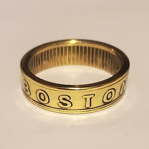 Peut inclure: Une bague dorée avec le mot "BOSTON" gravé autour de la bande.