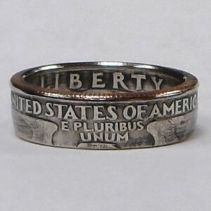 Puede incluir: Un anillo de plata hecho con una moneda de medio dólar estadounidense. El anillo presenta las palabras "Liberty", "United States of America", "E Pluribus Unum" y un retrato de una mujer.