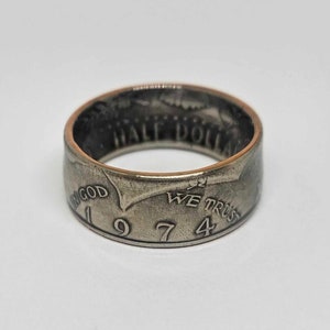 May include: A silver half dollar coin ring with the inscription "IN GOD WE TRUST" and the date "1974".