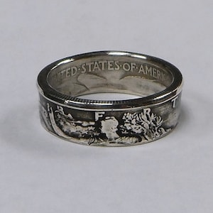 May include: A silver ring made from a US half dollar coin. The ring features the image of a bald eagle with outstretched wings and the inscription "UNITED STATES OF AMERICA".