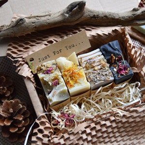 old process soap in a box. 4 bars naturally coloured with clays, flowers and roots. One lilac, one black, one yellow and one blue bar. Pretty flowers on top. Packaged with eco wood shavings. There is a note which says 'just for you'.