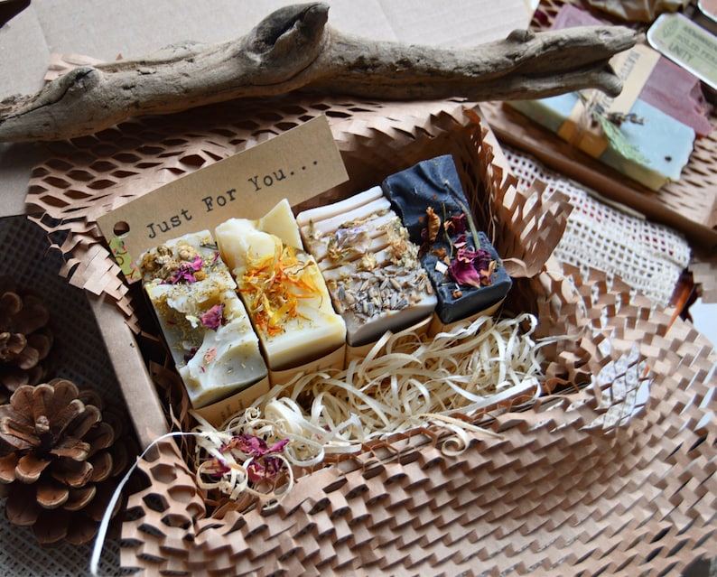 old process soap in a box. 4 bars naturally coloured with clays, flowers and roots. One lilac, one black, one yellow and one blue bar. Pretty flowers on top. Packaged with eco wood shavings. There is a note which says 'just for you'.