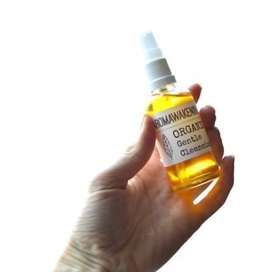 K&ouml;nnte beinhalten: Eine durchsichtige Glasspr&uuml;hflasche gef&uuml;llt mit einer goldgelben Fl&uuml;ssigkeit. Das wei&szlig;e Etikett tr&auml;gt den Text AROMAWAKENING, ORGANIC und Gentle Cleansing sowie eine kleine Strichzeichnung eines Blattes. Die Flasche hat einen wei&szlig;en Pumpkopf.