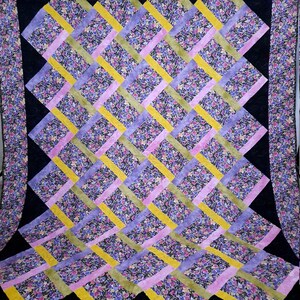 May include: A quilt with a black background and a pattern of overlapping squares in shades of purple, pink, yellow, and green. The squares are made of a floral fabric with a small, delicate pattern.