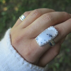 May include: A silver ring featuring a rectangular white and grey stone set in a silver bezel. The stone has a natural, rough texture.