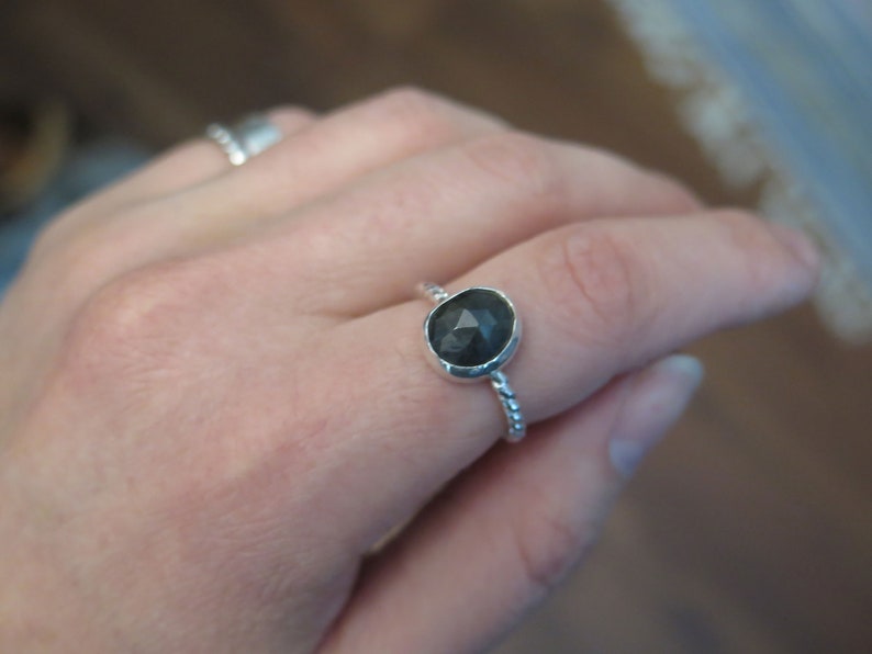 K&ouml;nnte beinhalten: Ein silberner Ring mit einem dunkelgrauen Edelstein. Der Ring hat ein gedrehtes Band.