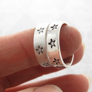 May include: Two silver rings with a brushed finish and cut-out star designs. The rings are stacked on top of each other.