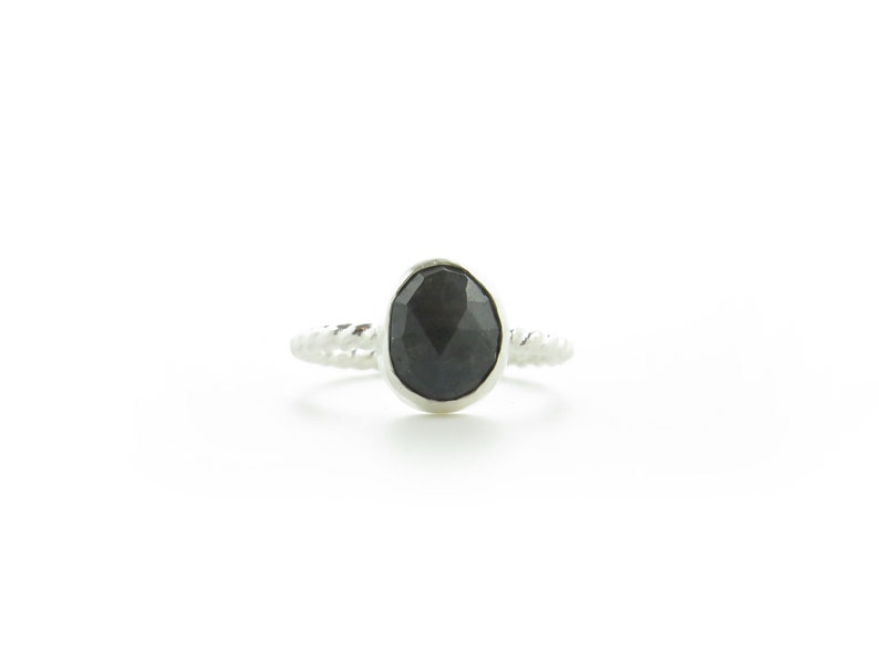 K&ouml;nnte beinhalten: Ein silberner Ring mit einem schwarzen Edelstein. Der Ring hat ein gedrehtes Band.