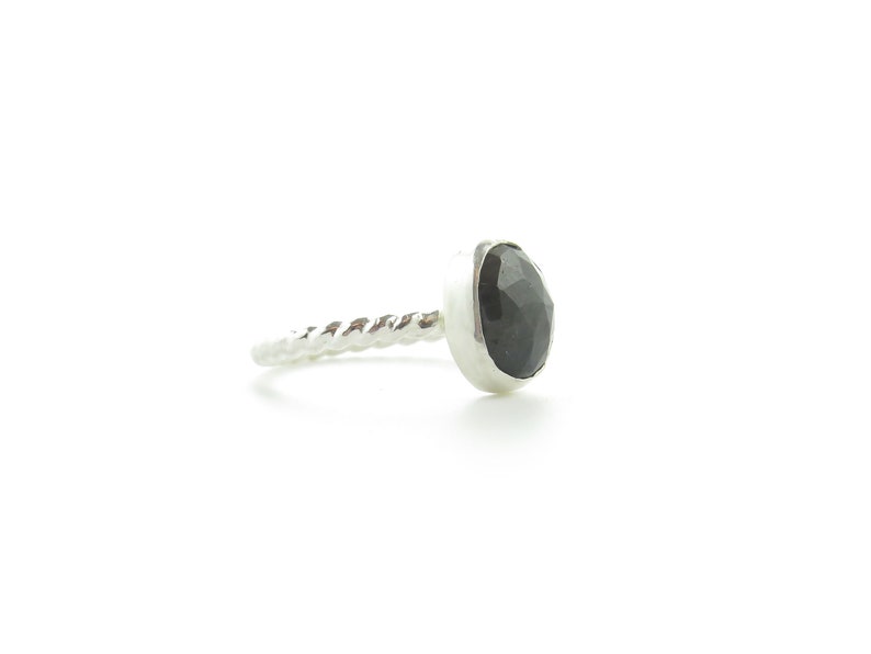 K&ouml;nnte beinhalten: Ein silberner Ring mit einem gedrehten Band und einem schwarzen Edelstein, der in einer Zargenfassung sitzt.