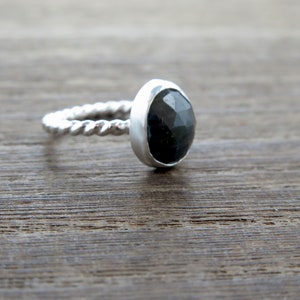K&ouml;nnte beinhalten: Ein silberner Ring mit einem gedrehten Band und einem dunkelgrauen Edelstein.