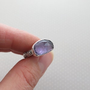 May include: A silver ring with a large, rectangular, faceted amethyst gemstone. The ring has a detailed, ornate band.