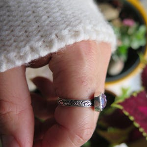 May include: A silver ring with a purple gemstone set in a floral design.