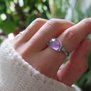 May include: A silver ring with a purple amethyst gemstone. The ring has a delicate floral design on the band.