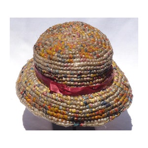 May include: A woven straw hat with a wide brim and a red ribbon. The hat is made of a variety of colors and textures, including brown, yellow, orange, and blue.