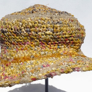 May include: A yellow, brown, and white woven hat with a wide brim. The hat is made of recycled materials and has a unique, textured surface.