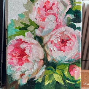 May include: A close-up of a painting of pink peonies with green leaves. The painting is on a canvas and is framed.