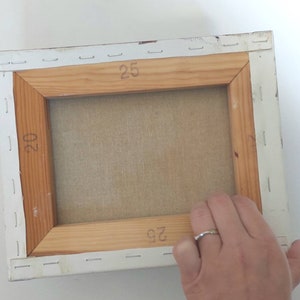 May include: The back of a stretched canvas painting with a wooden frame. The canvas is stapled to the frame and the dimensions are marked on the frame: 20 x 25 inches.