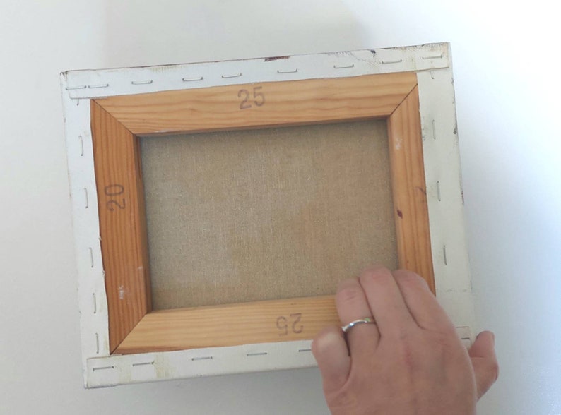 May include: The back of a stretched canvas painting with a wooden frame. The canvas is stapled to the frame and the dimensions are marked on the frame: 20 x 25 inches.