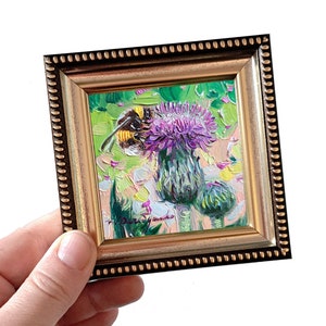 May include: A small framed painting of a bumblebee on a purple thistle flower. The painting is done in a vibrant style with thick brushstrokes. The frame is gold with a beaded edge.