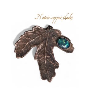 May include: A bronze-colored leaf-shaped brooch with an oval, iridescent, teal-colored stone. The brooch has detailed veining and the text "Nature copper shades" in a cursive font.