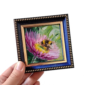 May include: A small framed painting of a bumblebee on a pink flower. The painting is in a blue and gold frame.