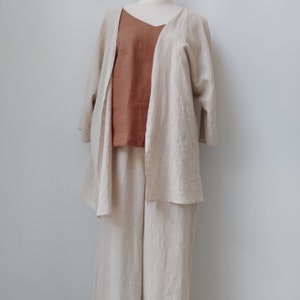 May include: A beige linen cardigan with a brown linen tank top underneath. The cardigan has a relaxed fit and a long, flowing silhouette. The tank top has a scoop neck and a loose fit.