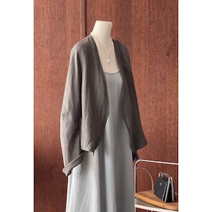 Pode incluir: Um cardigã de linho cinza com uma frente drapeada e mangas compridas. O cardigã é usado sobre um vestido azul claro.