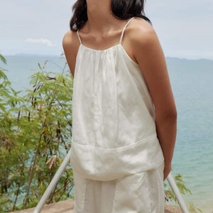 May include: A white sleeveless top with a gathered neckline and a relaxed fit. The top is made of a lightweight fabric and has a casual, summery feel.