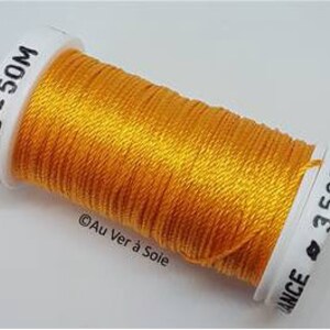 May include: A spool of bright yellow thread with white labels. The labels display the text "20ND-50M" and "3521". The thread is labeled "Au Ver à Soie".