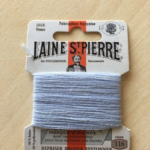 May include: A spool of light blue embroidery floss with a white label that reads "LAINE STPIERRE Ets TOULEMONDE Successeurs MARQUE STPIERRE sont recommandées pour tous les travaux de Dames REPRISER BRODER FESTONNER coloris 116". The label also states "50% laine 50% polyamid" and "Fabrication française".