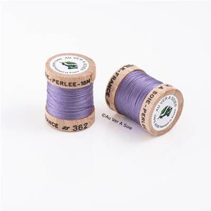 Peut inclure: Deux bobines de fil de couleur lavande enroulées sur des bobines en bois. Les bobines sont étiquetées "Au Ver A Soie" et "Perlee-15N".