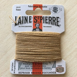 May include: A spool of Laine St. Pierre thread, color 370, with a white and orange label. The label reads "Fabrication française" and "REPRISER BRODER FESTONNER". The thread is a light brown color and is made of 50% wool and 50% polyamide.