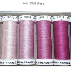 May include: Six spools of thread in various shades of pink and purple, labeled "Soie 1003 Rose" and "AU VER A SOIE-100% SOIE/SILK-FRANCE".