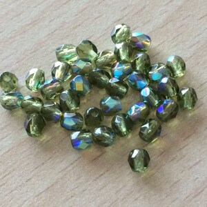 May include: A pile of green iridescent glass beads. The beads are faceted and have a shimmery finish.