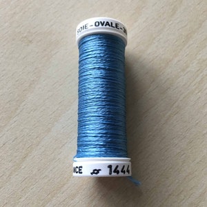 Peut inclure: Une bobine de fil bleu avec une étiquette blanche qui indique "SOIE - OVALE - 30" et "ANCE # 1444".