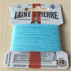 May include: A spool of light blue yarn labeled "LAINE STPIERRE" with the text "LES LAINES MARQUE STPIERRE sont recommandées pour tous les travaux de Dames" and "REPRISER BRODER FESTONNER". The label also states "50% laine 50% polyamide" and "coloris 16".