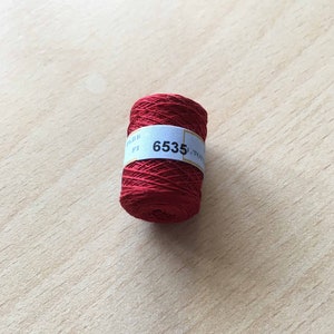 Può includere: Un'bobina di filo da ricamo rosso con un'etichetta bianca su cui è scritto "6535".