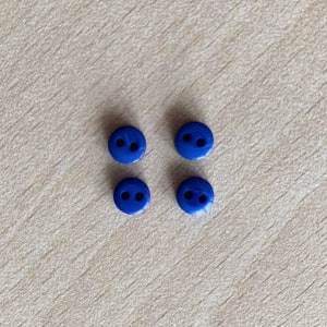 Pode incluir: Quatro botões pequenos de plástico azul com dois furos cada.