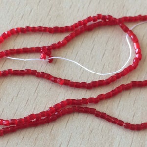Può includere: Un filo di perline di vetro rosse, infilate su un filo bianco, è disposto a forma di cerchio sciolto.